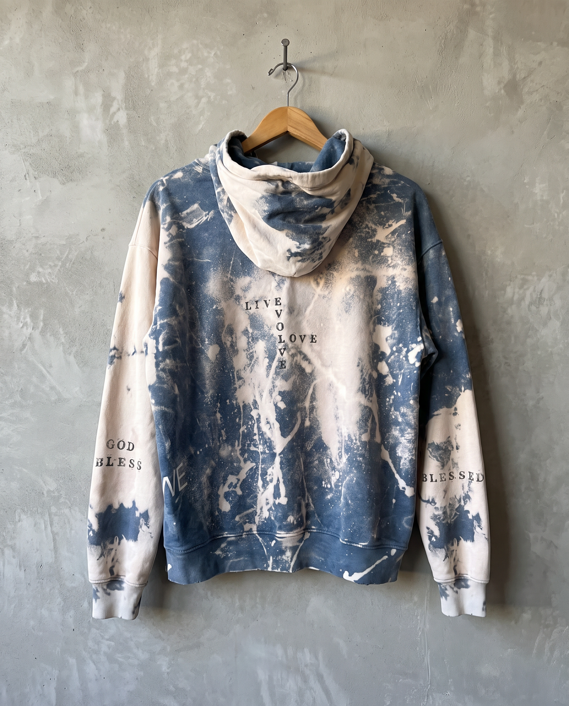 Every Bit of It sweatshirt in faded blue, hand-bleached finish, hanging on a wooden hanger against a textured gray concrete wall, featuring collage-style text and graphic print.