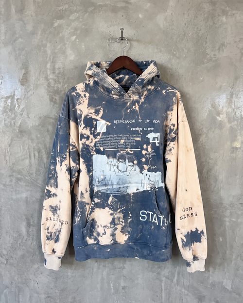 Every Bit of It sweatshirt in faded blue, hand-bleached finish, hanging on a wooden hanger against a textured gray concrete wall.